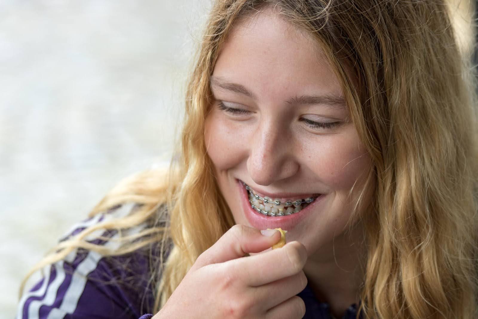 young woman eating a snack with braces on how long does it take to get used to braces callan rothodontics