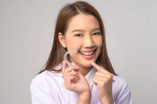 female patient smiles while holding up clear aligners callan othodontics