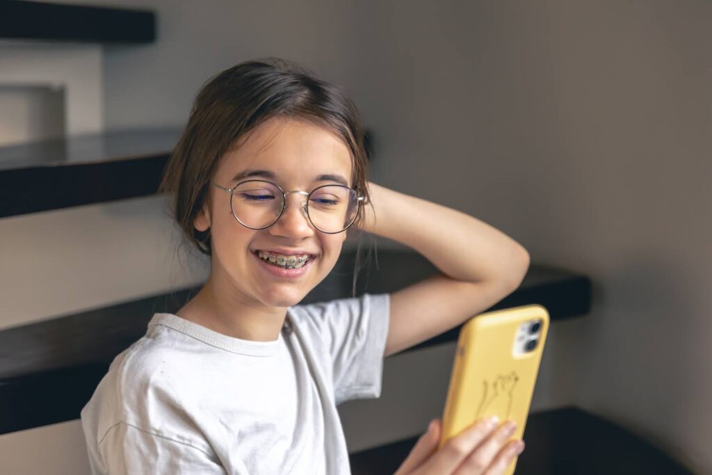 young female patient looking at phone and smiling with braces braces vs invisalign